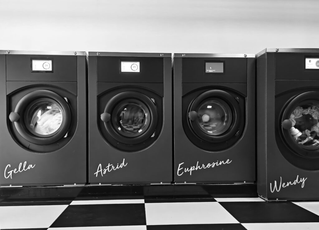 صيانة الغسالات Grayscale image of four modern washing machines in a self-service laundry.
