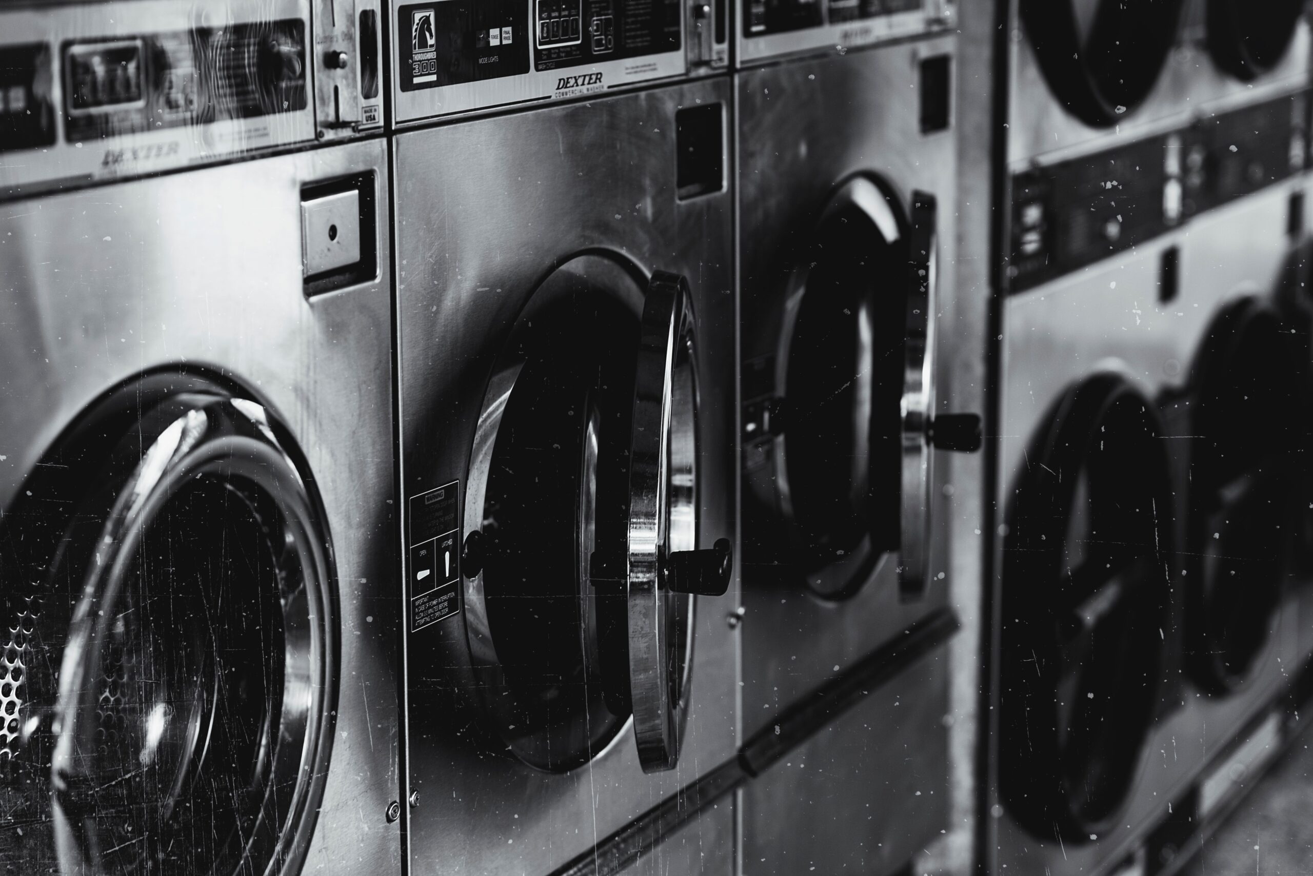 صيانة الغسالات Black and white image of industrial washing machines in a retro style laundry facility.