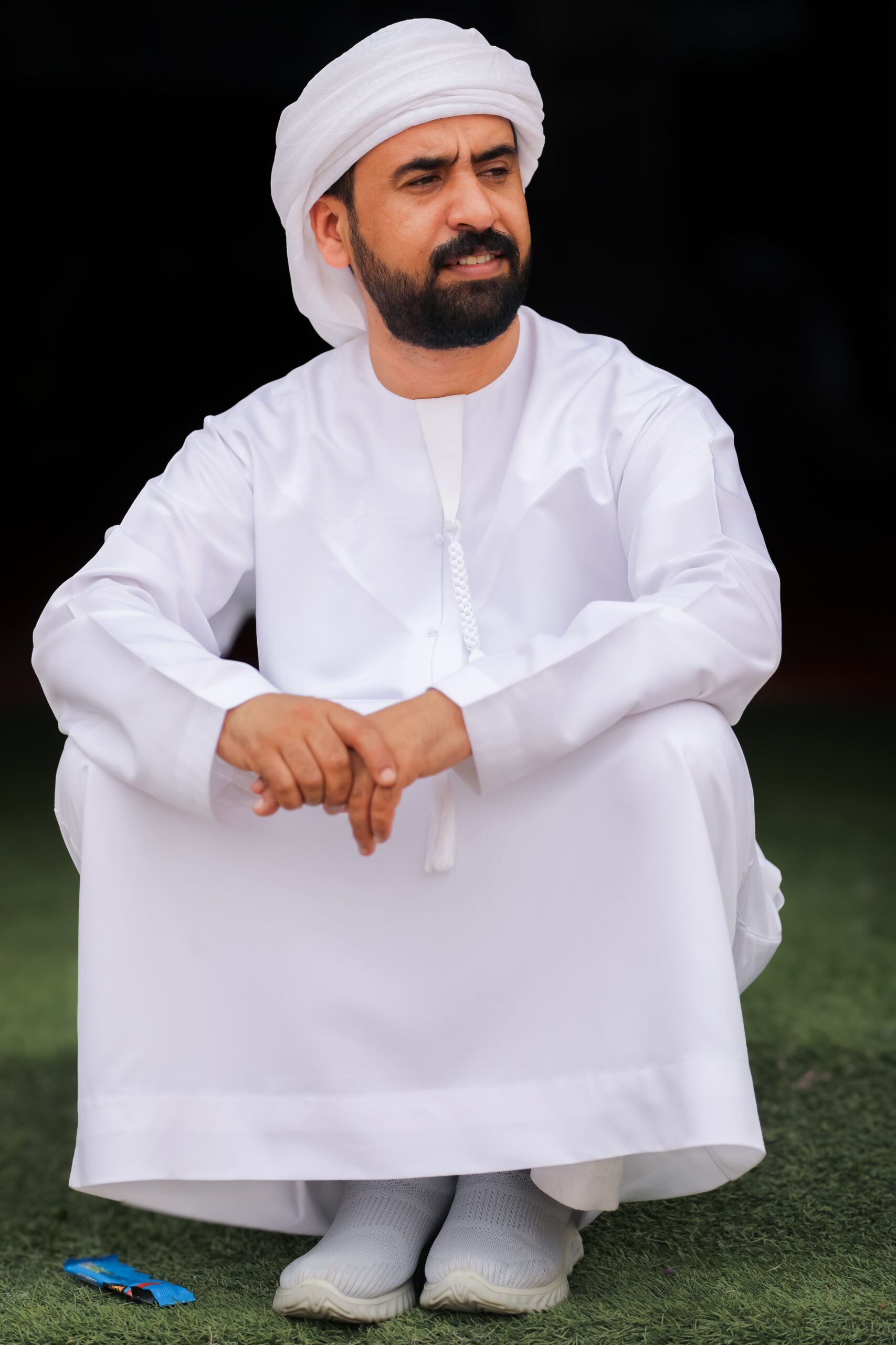 صيانة الغسالات Man wearing traditional Middle Eastern clothing, sitting outdoors on grass.