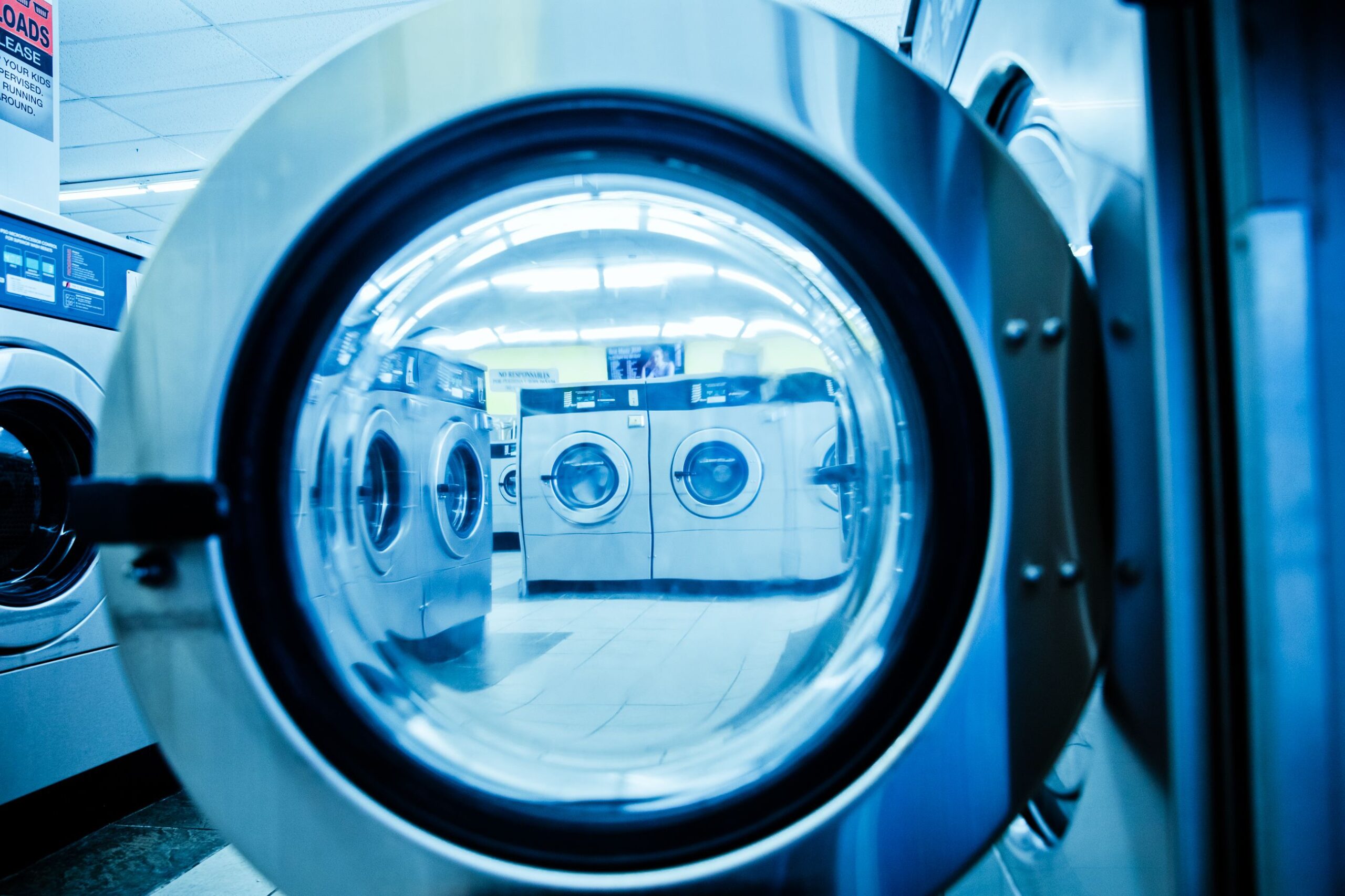 صيانة الغسالات Interior view of a modern laundromat with rows of steel washing machines.