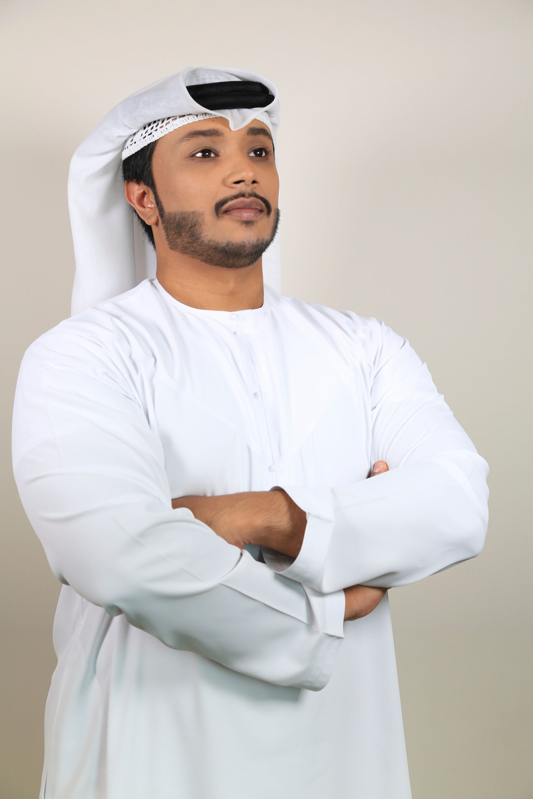 صيانة الغسالات Portrait of a Middle Eastern man in traditional attire with arms crossed, studio shot.